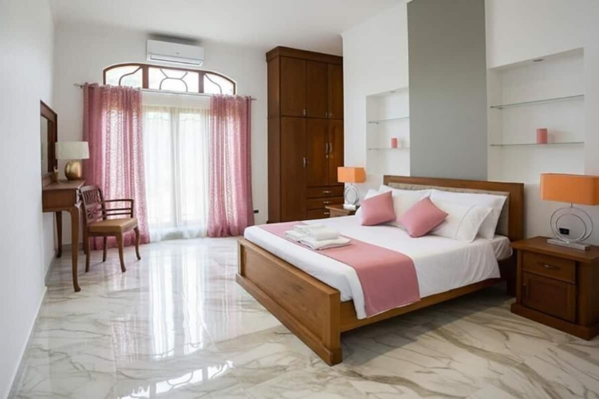 A bedroom with a bed, bedside tables, a desk, a chair, a wardrobe, and a window with curtains.