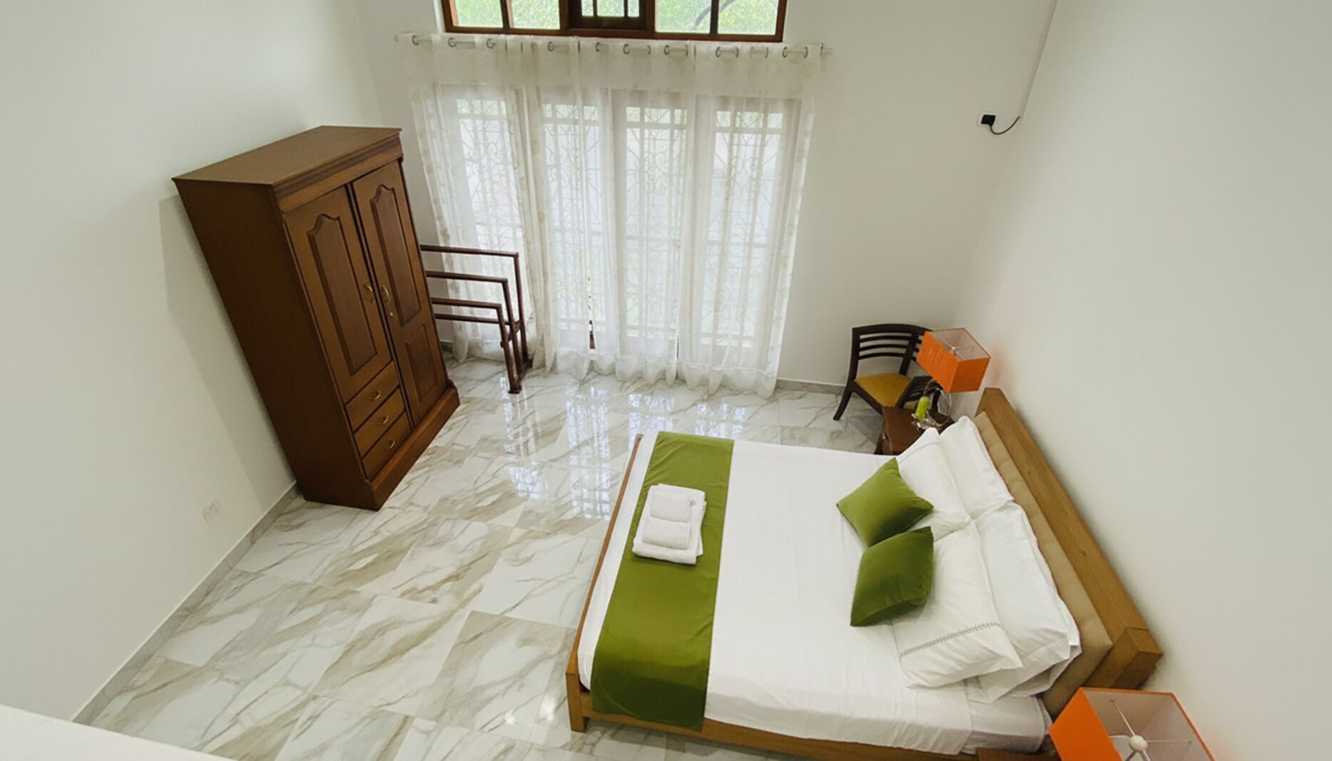 Un dormitorio con cama, armario, silla y ventana con cortinas.