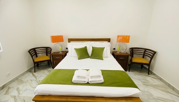 A hotel room with a bed, two nightstands, two chairs, and a marble floor.