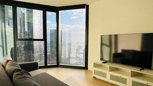 Una sala moderna con un sofá grande, un televisor de pantalla plana y vistas a la ciudad a través de ventanales del suelo al techo.