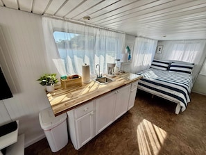 A compact kitchen with a wooden countertop, a sink, and a window with sheer curtains.