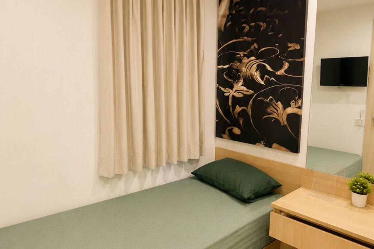 Ein kleines, ordentlich eingerichtetes Schlafzimmer mit einem Einzelbett, einem Nachttisch, einem Spiegel und einem an der Wand montierten Fernseher.