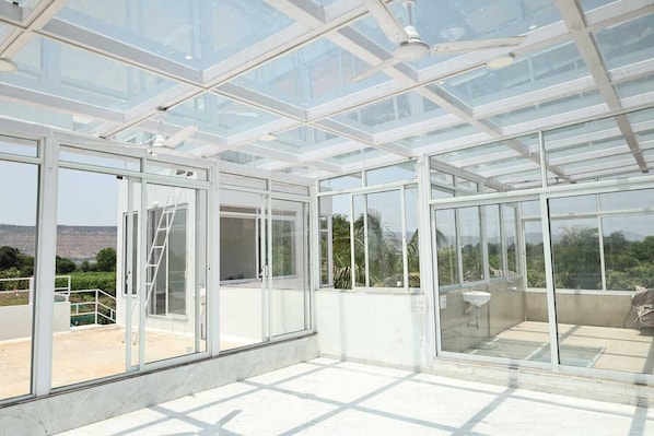 A large glass-enclosed space with multiple sliding glass doors, a white ceiling, and a view of the outdoors.