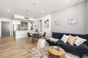 Ein modernes Wohnzimmer mit einem dunkelgrauen Sofa, einem runden Holztisch und einem Essbereich mit weißem Tisch und Stühlen.