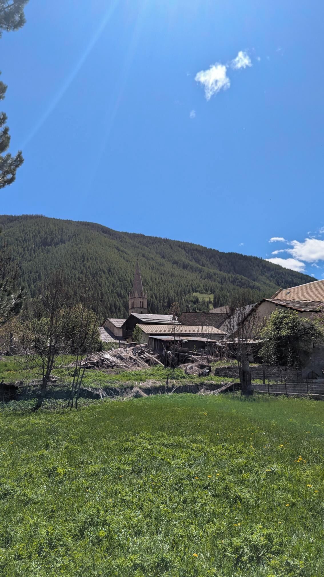 Un pueblo rural con edificios tradicionales, una iglesia y una montaña boscosa al fondo.