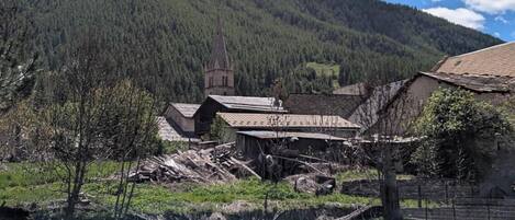 Un pueblo rural con edificios tradicionales, una iglesia y una montaña boscosa al fondo.