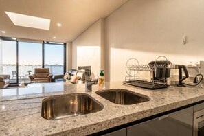 A modern kitchen with a large island, two sinks, and a view of the sea. - Stylish 2BR Olympic Park | Pool, Gym & Parking (Sydney Olympic Park)