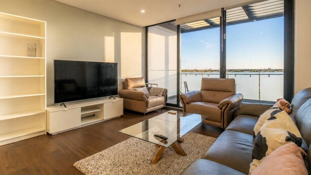 Ein modernes Wohnzimmer mit einem Flachbildfernseher, Ledersofas, einem Glastisch und einem großen Fenster mit Blick auf das Wasser.