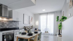 Eine moderne Küche mit Essbereich, weißen Wänden und einem großen Fenster mit durchsichtigen Vorhängen.
