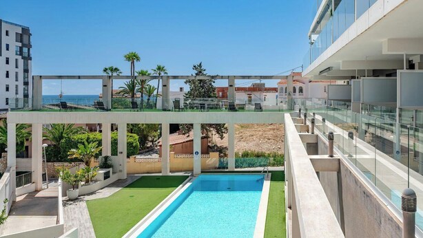 Ein Pool auf dem Dach mit freiem Blick auf das Meer, umgeben von modernen Gebäuden und Palmen.