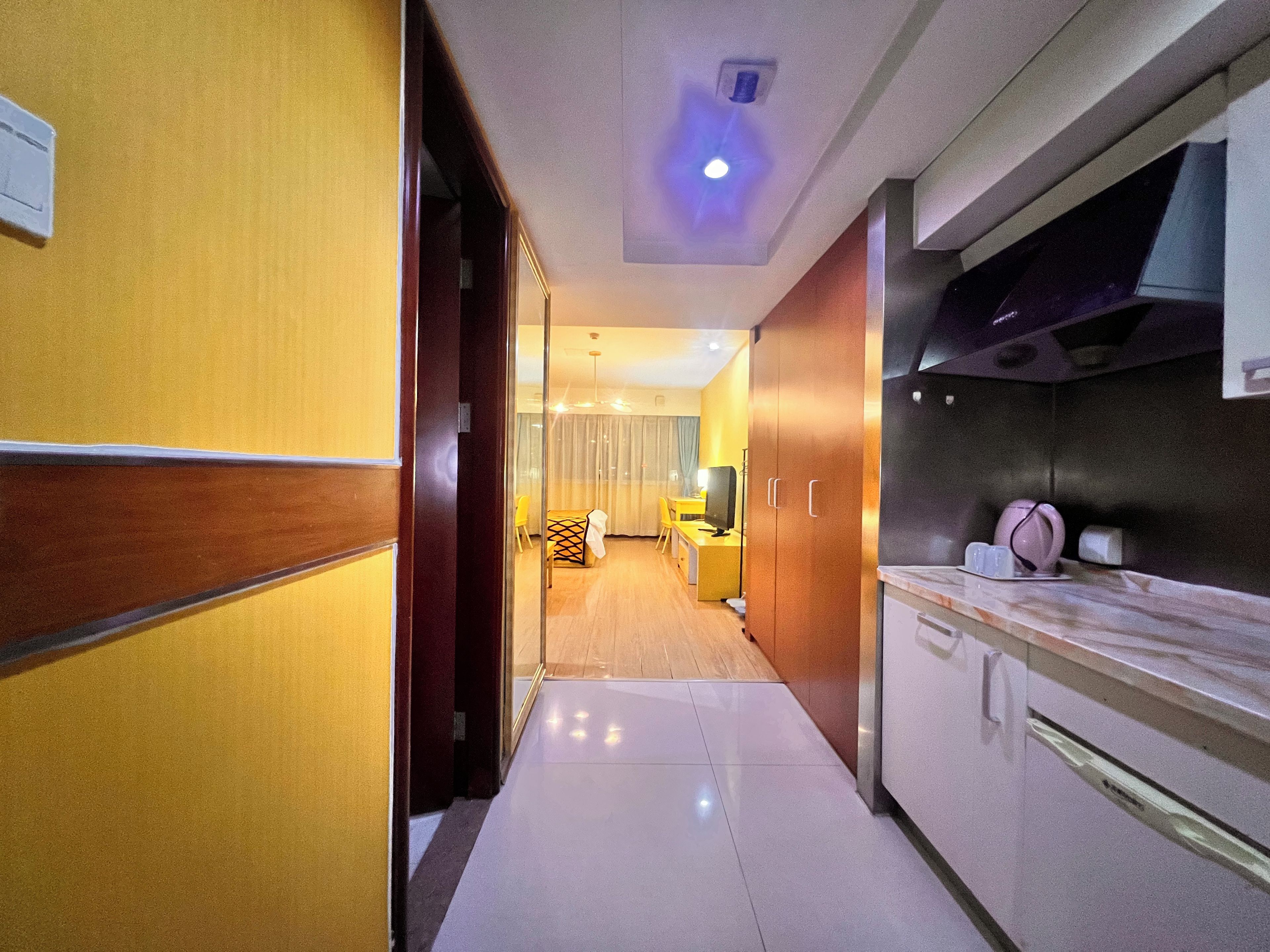 A hotel corridor with a kitchen area on the right, featuring cabinets and a countertop.