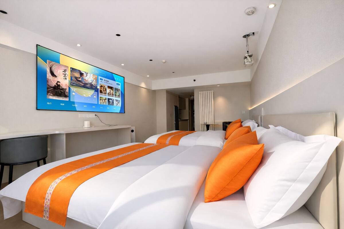 Una habitación de hotel moderna con una cama grande, un escritorio y un televisor mostrando una interfaz digital.