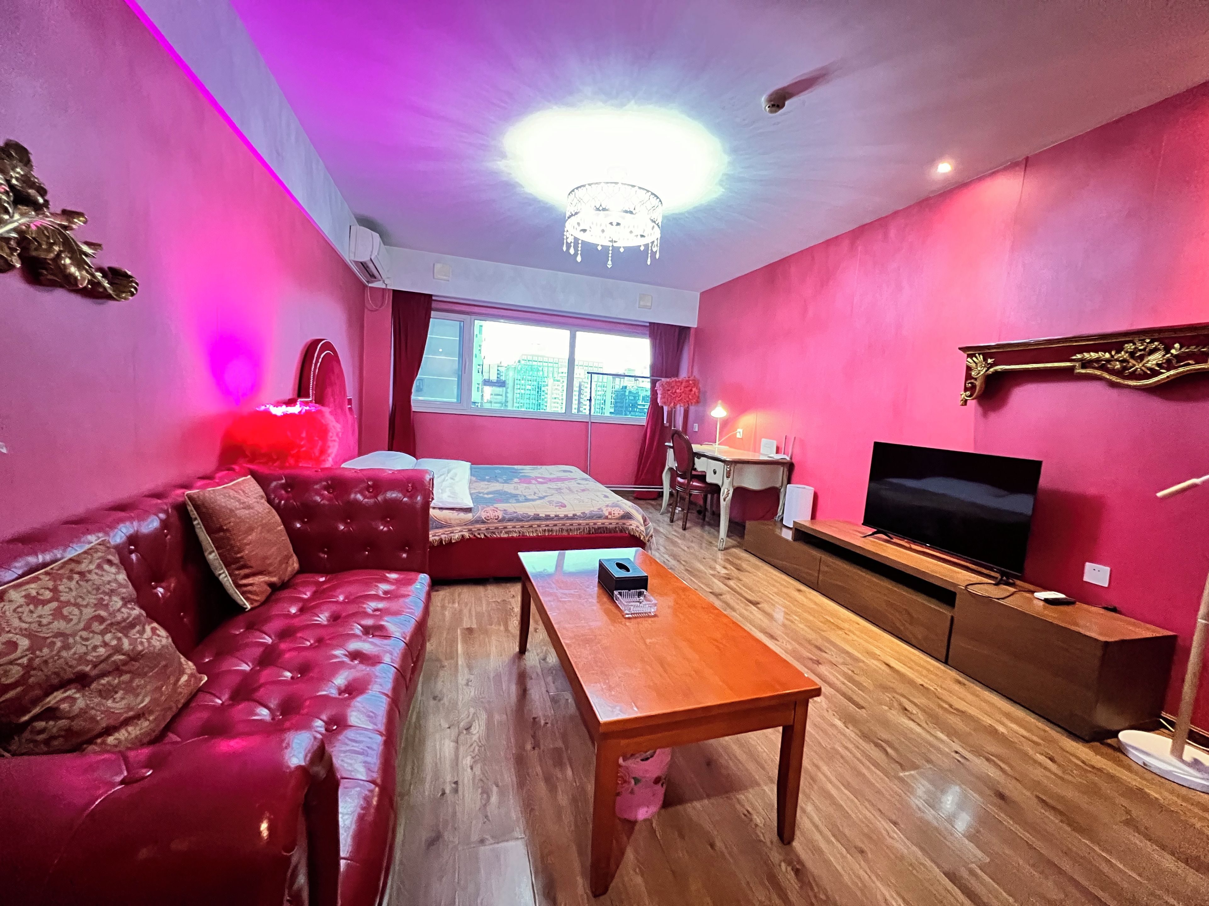A room with a red sofa, a wooden coffee table, a TV, and a desk with a chair.