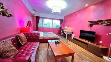 A room with a red sofa, a wooden coffee table, a TV, and a desk with a chair.