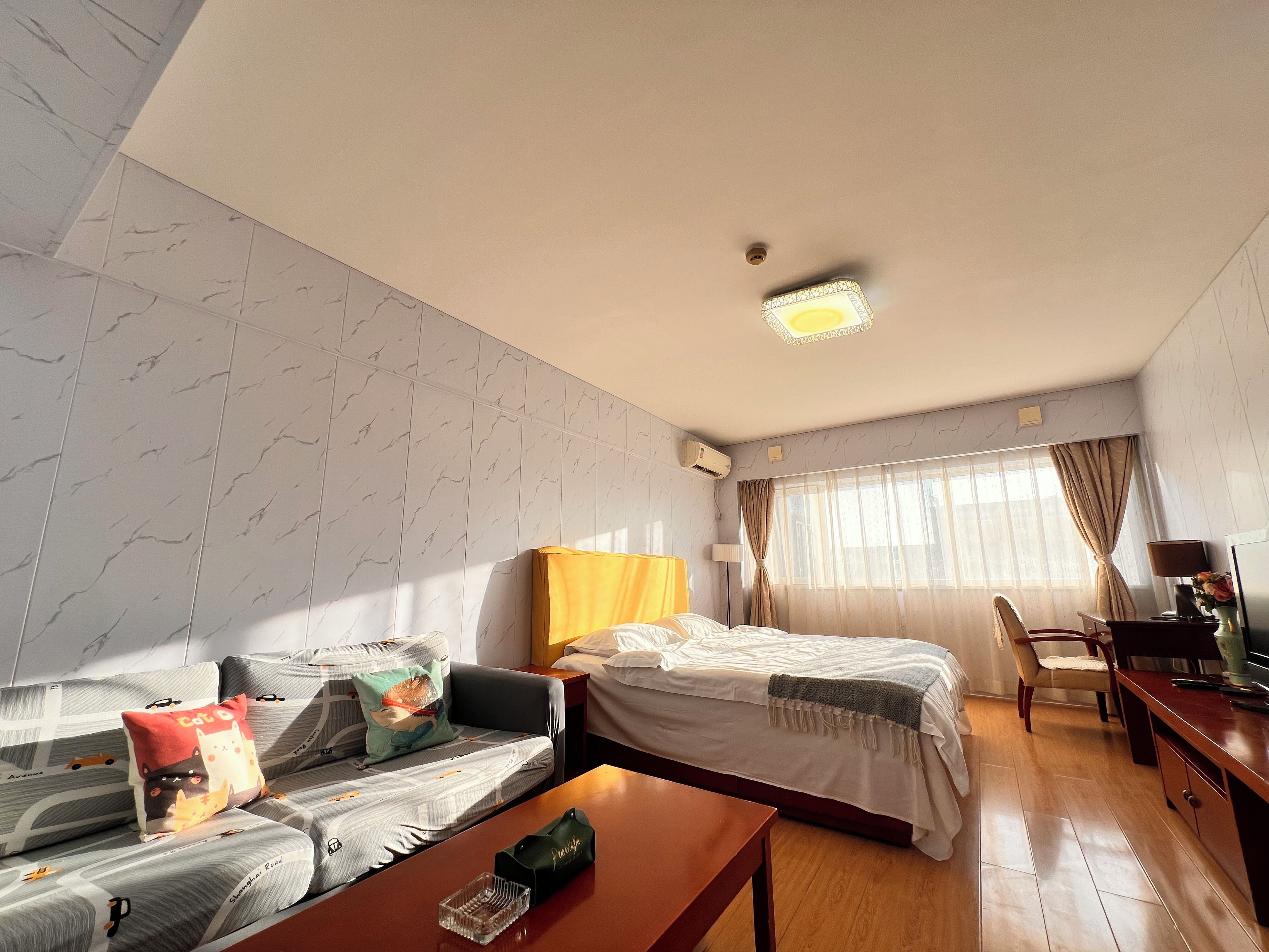 A hotel room with a sofa, bed, wooden table, and a desk with a lamp.