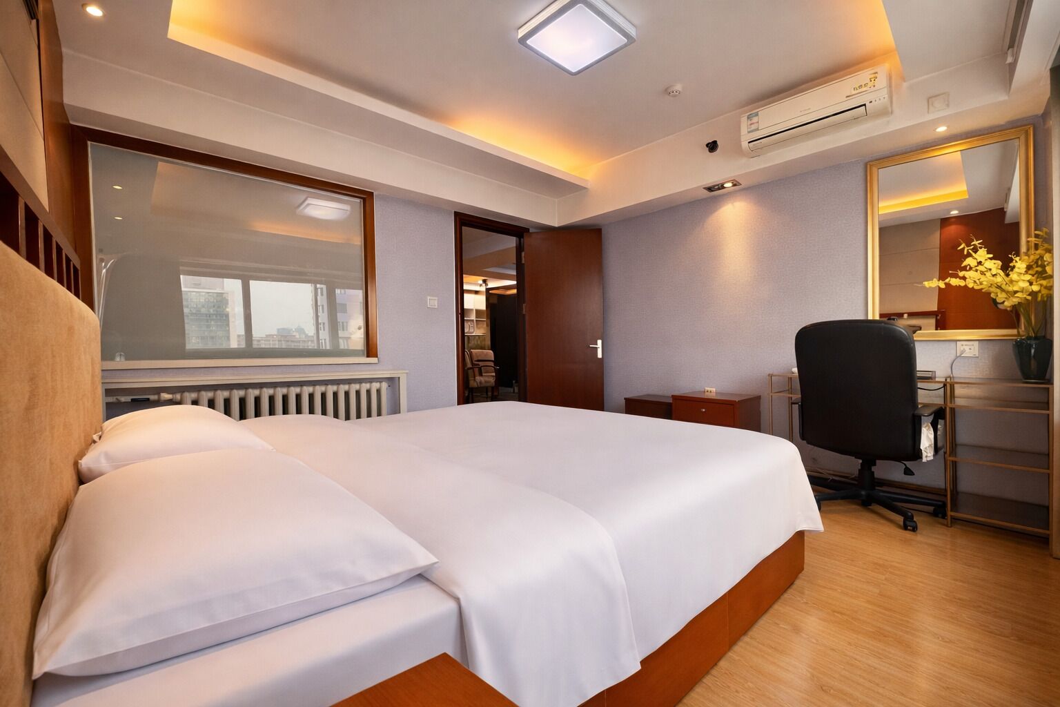 A hotel room with a bed, a desk, a chair, a radiator, and a window.