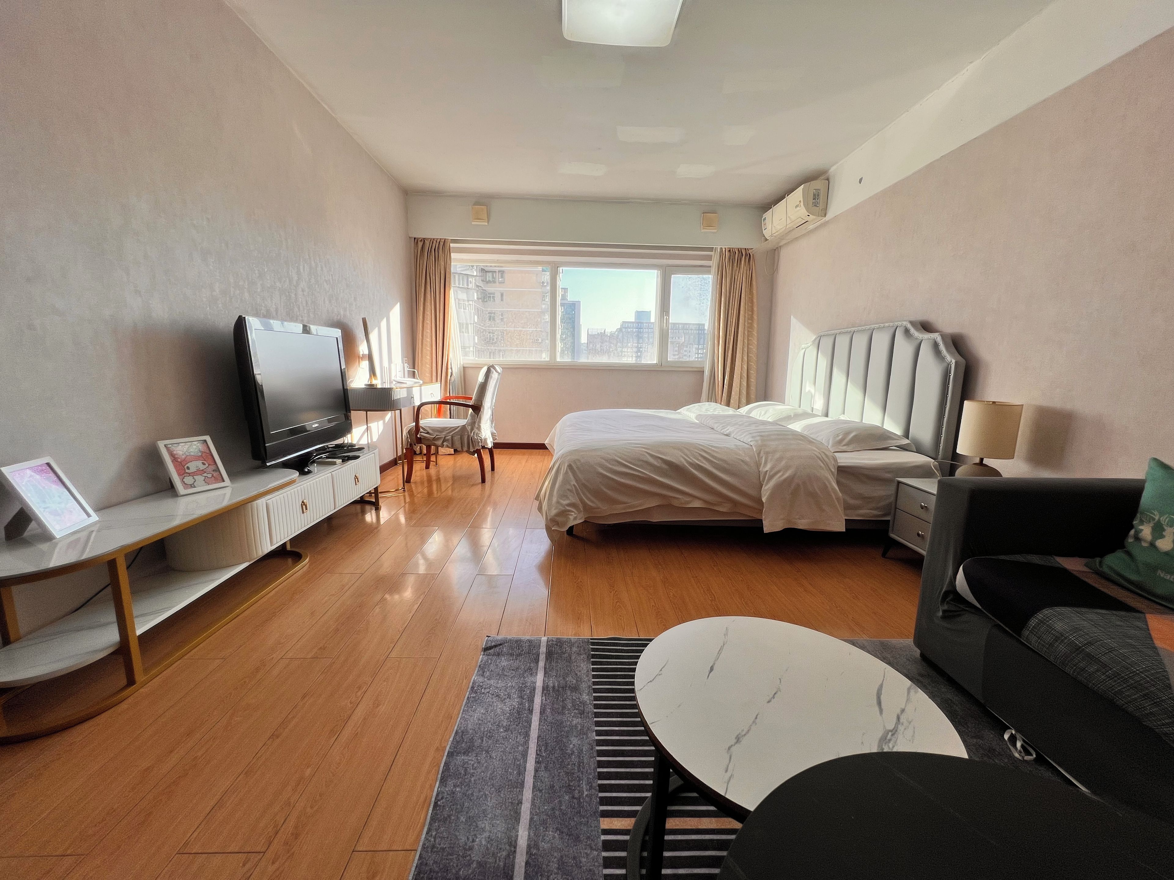 A hotel room with a bed, a TV, a desk, a chair, a sofa, and a view of the city.