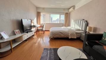 A hotel room with a bed, a TV, a desk, a chair, a sofa, and a view of the city.