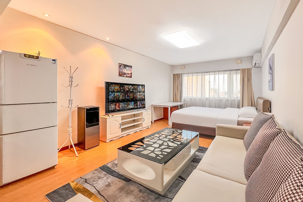 Habitación de hotel con cama, televisión, refrigerador, mesita de centro y sofá.