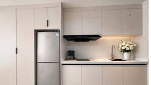 Une cuisine moderne dotée d’un réfrigérateur encastré en acier inoxydable, d’une hotte noire et d’un design minimaliste.