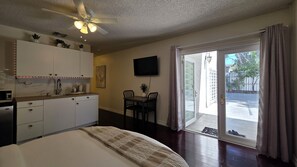 A hotel room with a bed, a kitchenette, a dining area, a TV, and a sliding glass door to the outside.