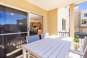 A balcony with a table and chairs, a sliding glass door leading to a kitchen, and a view of neighboring buildings. - Eight, Villa Mar Colina (Yeppoon)