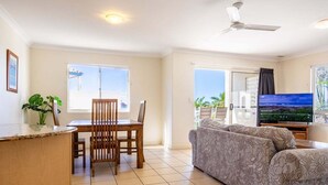 A living room with a dining area, a sofa, a TV, and a balcony with a view. - Eight, Villa Mar Colina (Yeppoon)