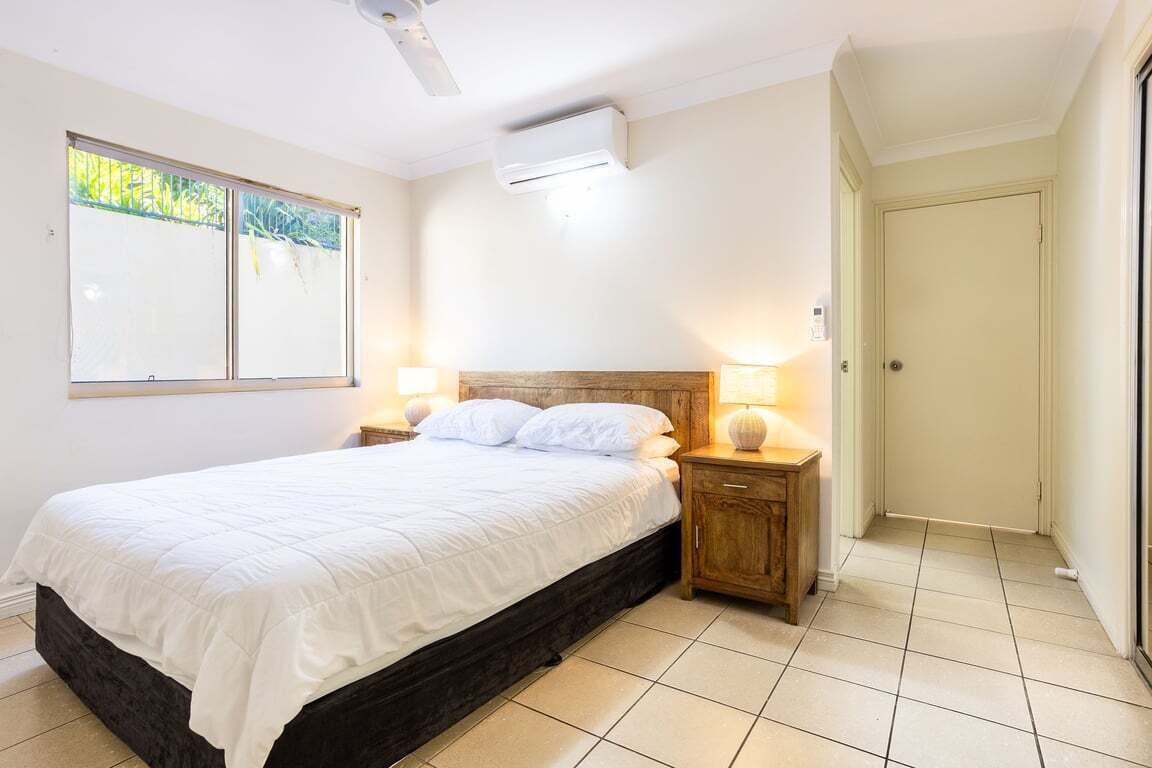 A bedroom with a bed, bedside lamps, a ceiling fan, and a window with blinds.