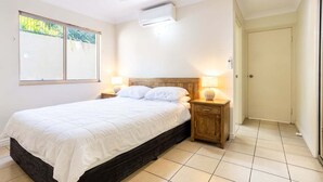 A bedroom with a bed, bedside lamps, a ceiling fan, and a window with blinds. - Eight, Villa Mar Colina (Yeppoon)