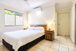 Ein Schlafzimmer mit einem Bett, Nachttischlampen, einem Deckenventilator und einem Fenster mit Jalousien.