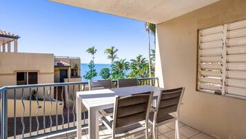 A balcony with a table and chairs, a view of the sea, and a building with a tiled floor.