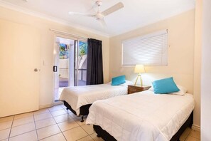 A hotel room with two beds, a ceiling fan, a window with blinds, and a door leading to a balcony. - Eight, Villa Mar Colina (Yeppoon)