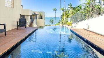 A swimming pool with a clear view of the ocean, a covered seating area, and a staircase leading to an upper level.