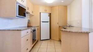 A compact kitchen with a microwave, refrigerator, oven, and a sink. - Eight, Villa Mar Colina (Yeppoon)