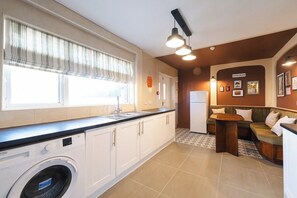 A compact kitchen with a washing machine, a dining area with a bench, and a wall-mounted light fixture.