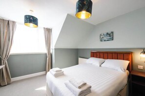 A hotel room with a bed, two bedside lamps, a nightstand, a window with curtains, and a wall-mounted picture.