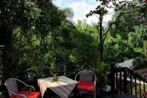 Eine Terrasse im Freien mit Tisch und Stühlen, umgeben von dichtem Grün.