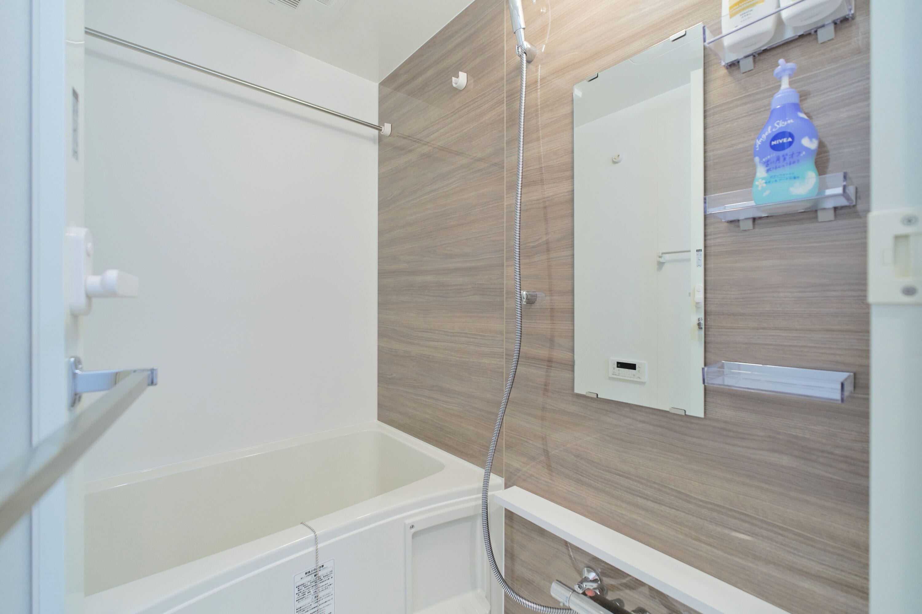 A bathroom with a bathtub, a shower, a mirror, and a soap dispenser on the wall.