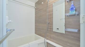A bathroom with a bathtub, a shower, a mirror, and a soap dispenser on the wall.