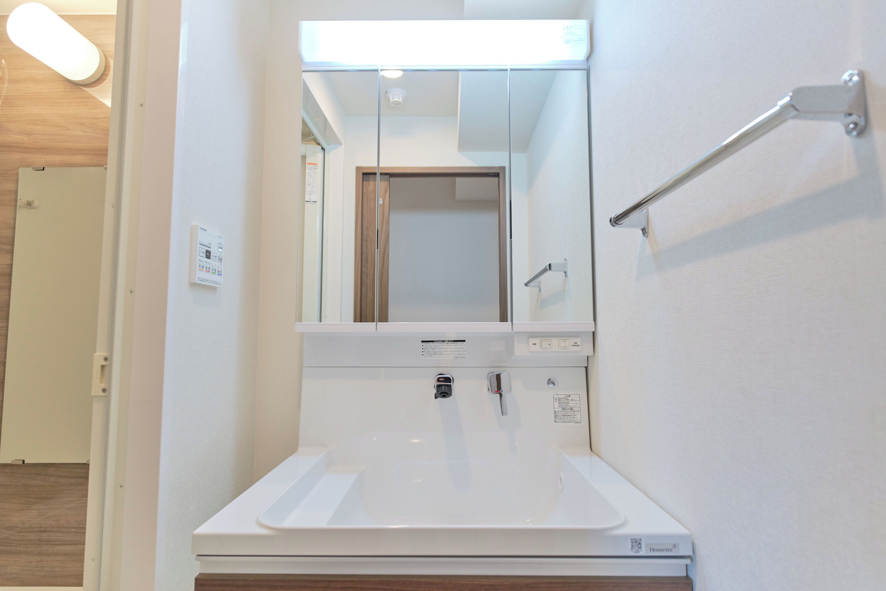 Un baño con lavamanos blanco, espejo y toallero.