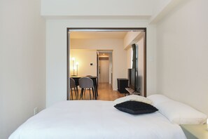 Una habitación de hotel con cama, escritorio con sillas, televisor y lámpara.