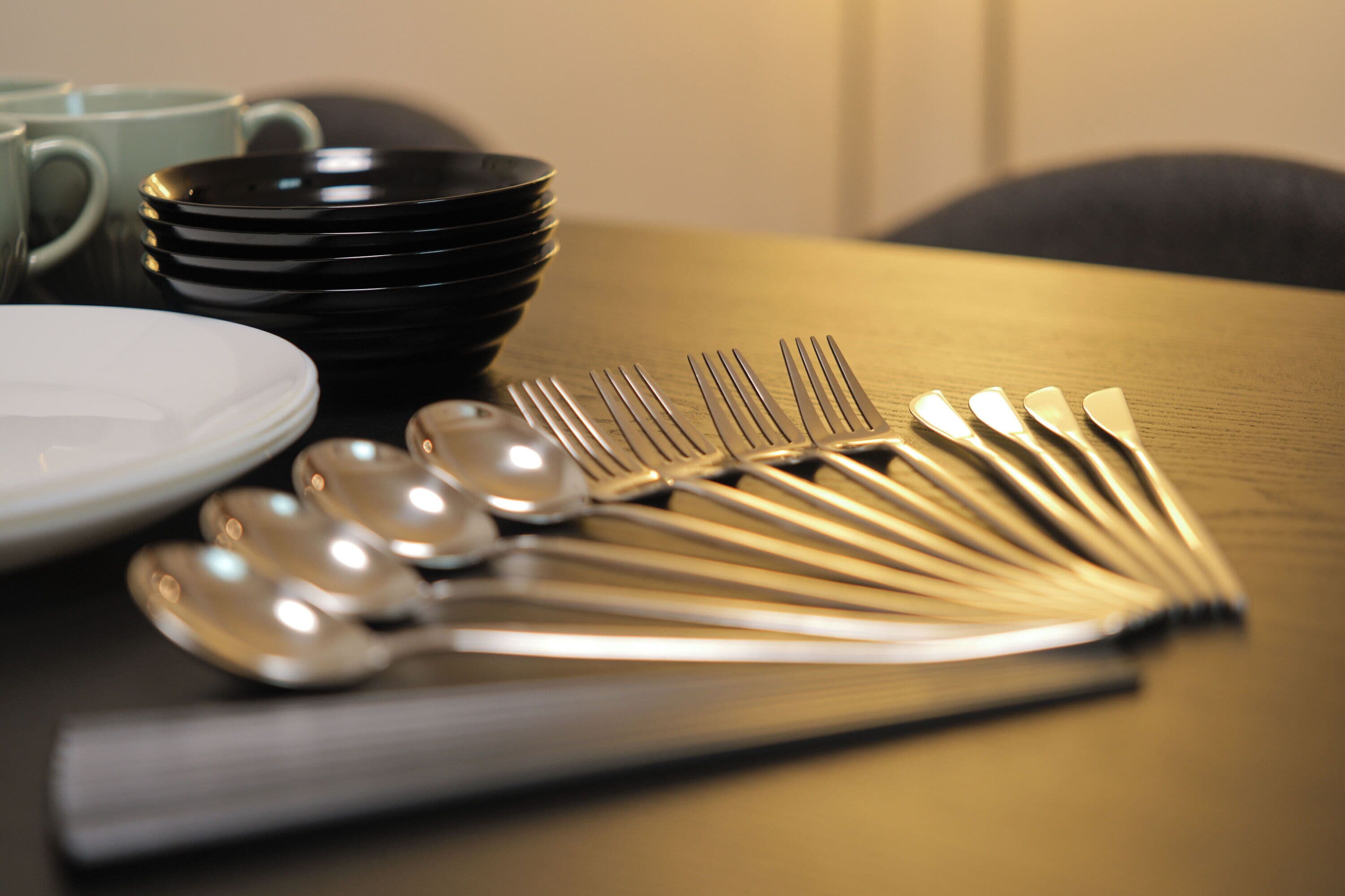 A table with a stack of black plates, a white plate, and a set of silverware.