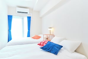 Quarto de hotel com duas camas, janela com cortinas, ar condicionado e mesa de cabeceira com luminária.