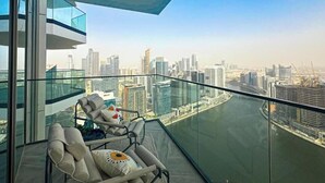 A balcony with a city view, a glass railing, and a chair with a cushion. - Luxury 1 BR with Stunning Water Views (Dubai)