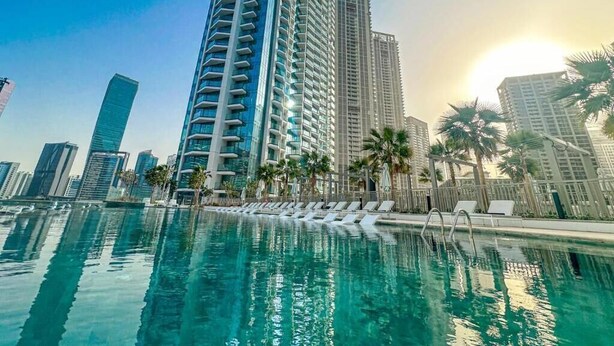 A swimming pool with lounge chairs, tall buildings, and palm trees in the background. - Luxury 1 BR with Stunning Water Views (Dubai)