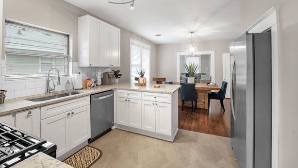 Een moderne keuken met witte kasten, een ingebouwde kookplaat en een eethoek met een houten tafel en stoelen.