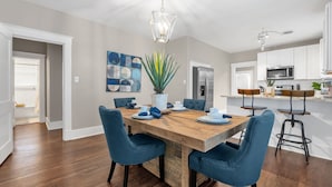 Een moderne keuken met witte kasten, een roestvrijstalen koelkast en een houten eettafel met blauwe stoelen.