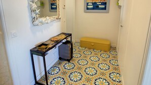 A hallway with a tiled floor, a console table with a suitcase, a mirror with a seashell frame, and a framed painting on the wall. - Apartment  by Interhome (Cannes)