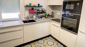 A compact kitchen with white cabinets, a black microwave, and a tiled backsplash. - Apartment  by Interhome (Cannes)