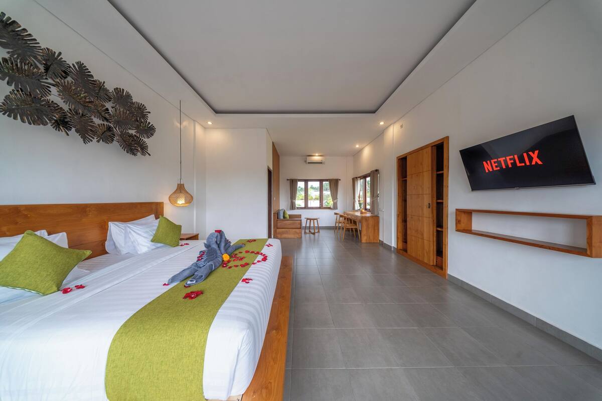 A modern hotel room with a bed, a TV, a desk, and a dining area.